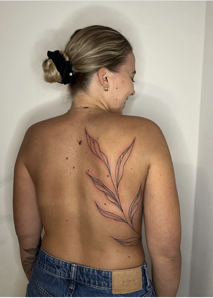 a woman with a tattoo on her back is standing in front of a white wall