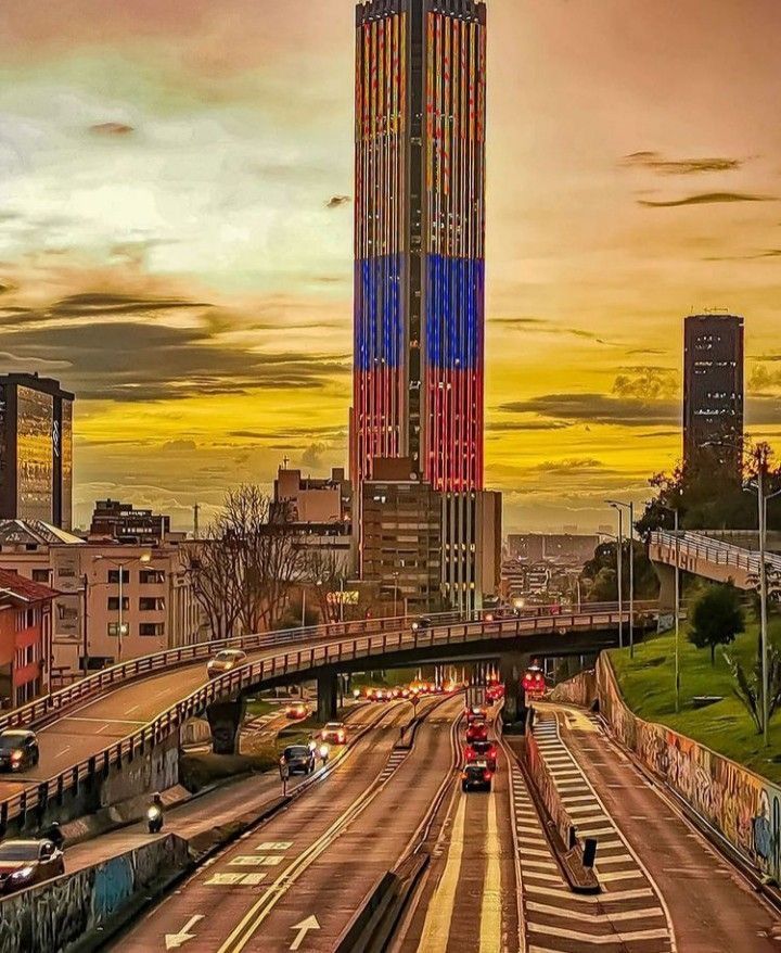 a very tall building towering over a city with traffic on the road below it at sunset