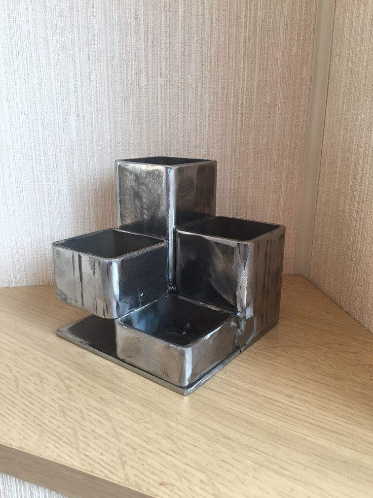 three square metal containers sitting on top of a wooden table next to a wallpapered wall