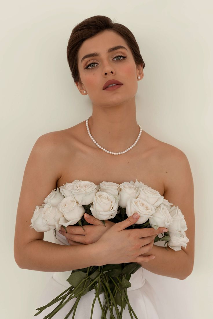 a woman in a white wedding dress holding a bouquet of flowers with pearls on her neck