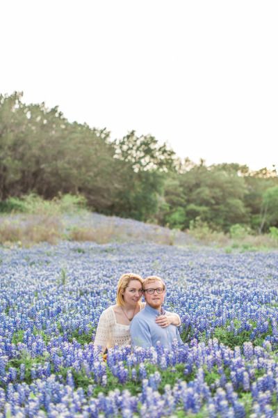 a man and woman sitting in a field of blue flowers