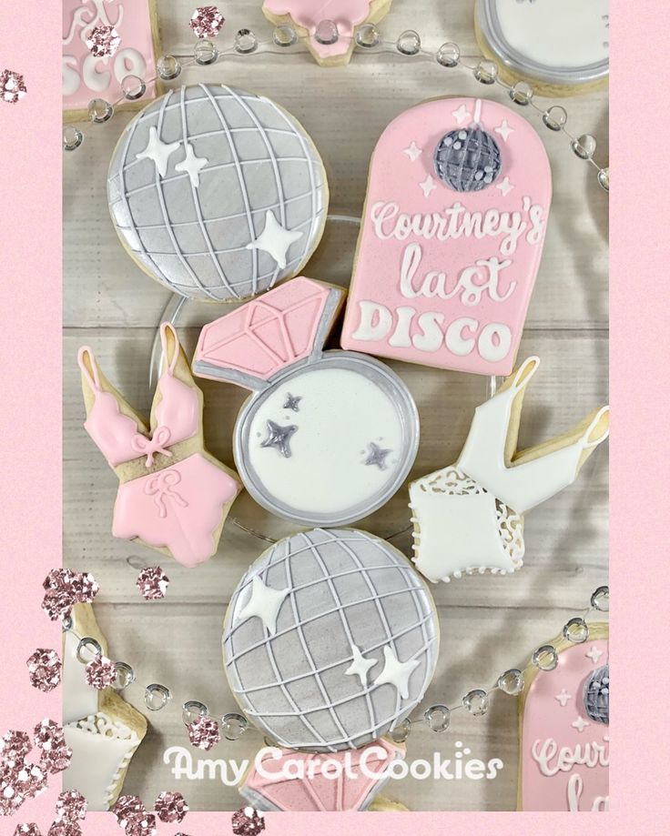 cookies decorated with pink and silver icing are arranged on a white table top, surrounded by other cookie decorating items