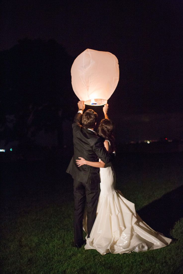 a bride and groom holding up a paper lantern