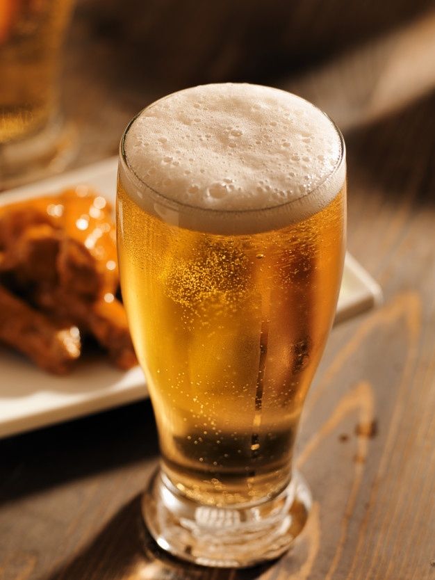 a glass of beer sitting on top of a wooden table next to some chicken wings