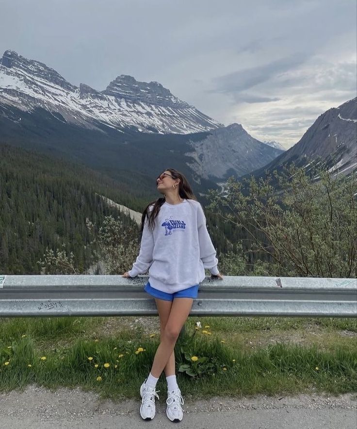 a woman is sitting on a bench looking up at the mountains and snow capped peaks