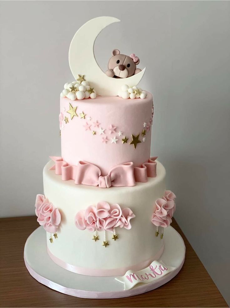 a pink and white cake with a teddy bear sitting on the top of it's tier