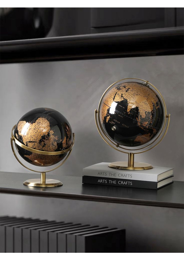 two black and gold globes sitting on top of a book shelf next to each other