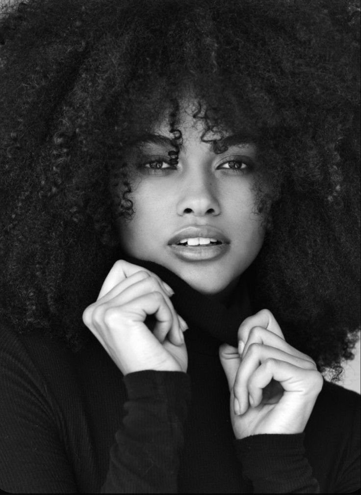 a woman with an afro is posing for a black and white photo, she has her hands on her chin