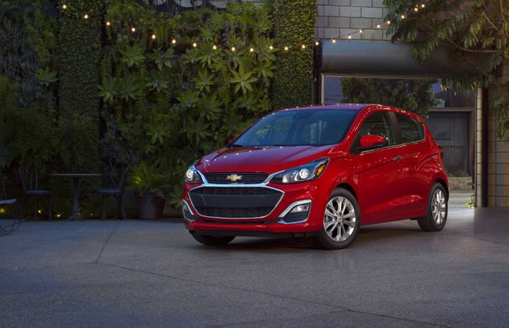 a red chevrolet spark is parked in front of a building with greenery on the walls