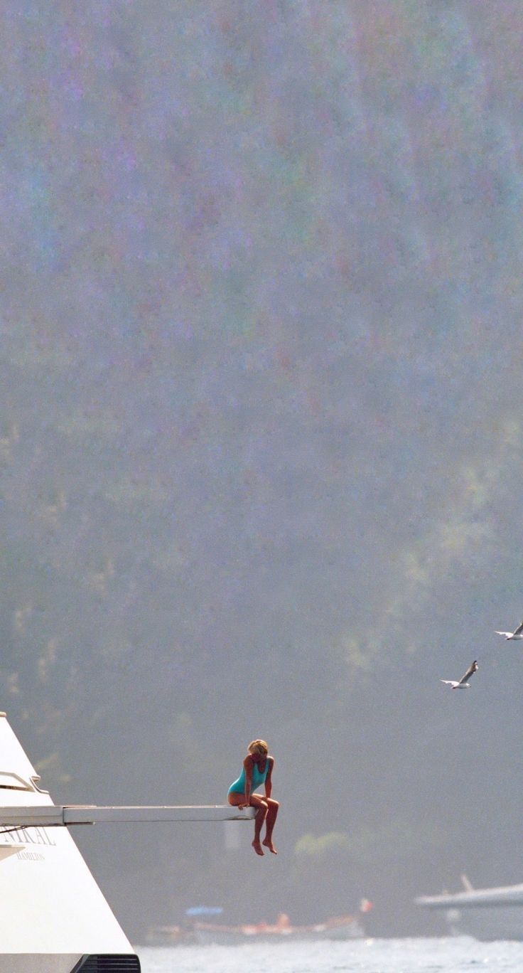 two people are sitting on a boat in the water and one person is standing up