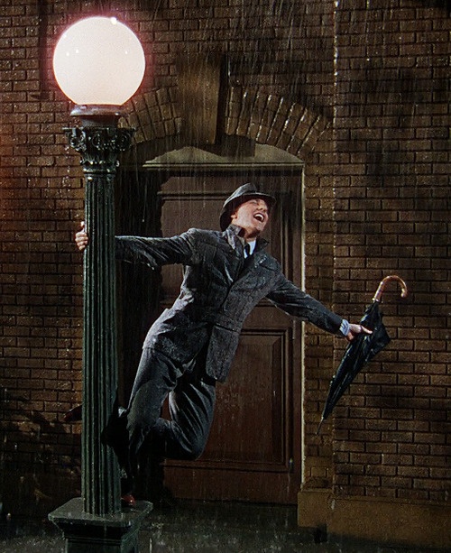 a man in a suit and hat holding an umbrella while standing on a lamp post