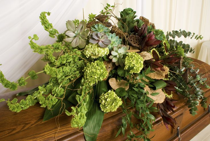 a bouquet of green and purple flowers sitting on top of a wooden bench next to a white curtain