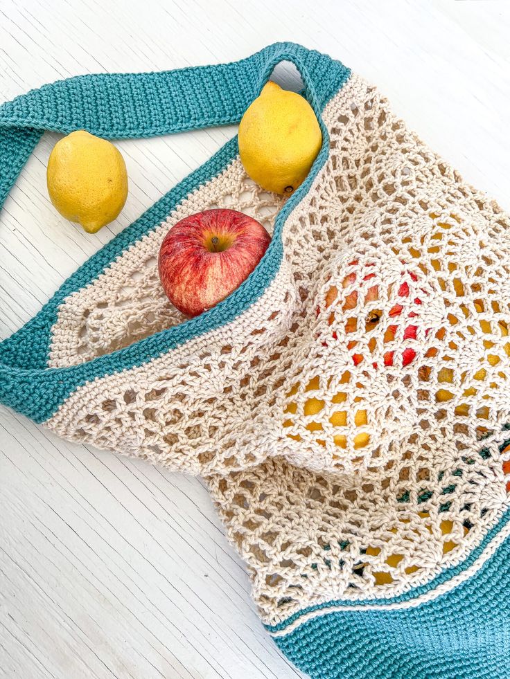 a crocheted bag with apples, lemons and an apple in it on a white table