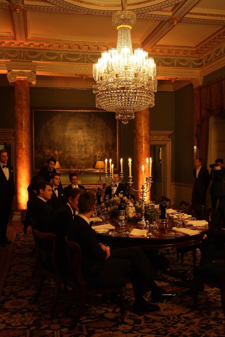 a group of people sitting around a table in a room with chandelier above it