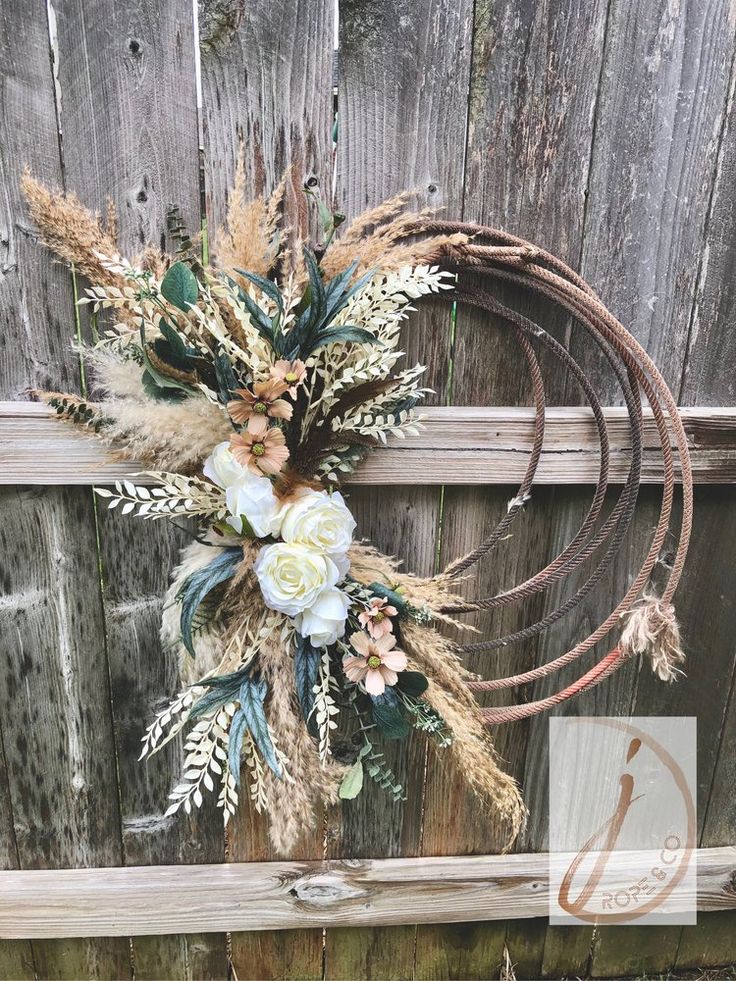 a wreath with flowers and leaves hanging on the side of a wooden fence next to a sign