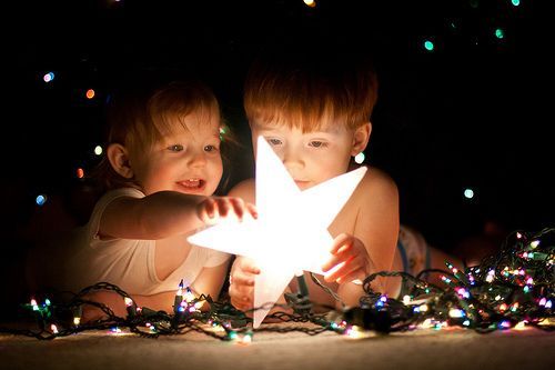 two young children are looking at a star in the dark with christmas lights all around them