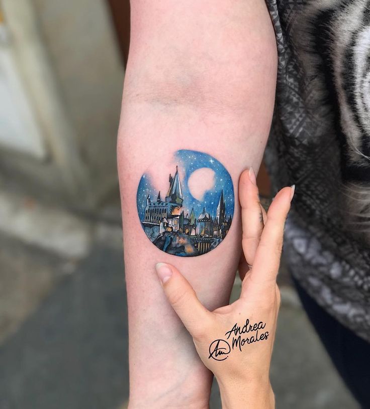 someone holding their arm up with a tattoo on it's left hand and the image of hogwarts castle