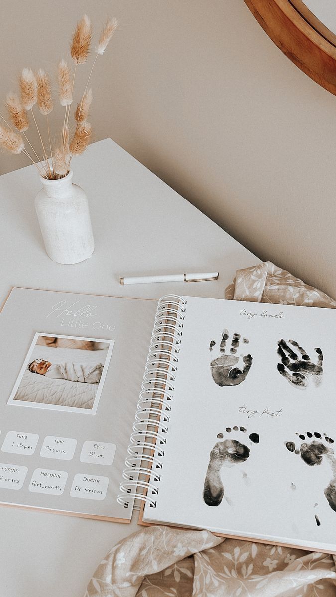 an open notebook with hand and foot prints on it next to a pen, flower vase and mirror