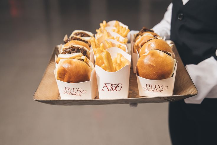 a tray that has some sandwiches and french fries on it, with the waiter in the background