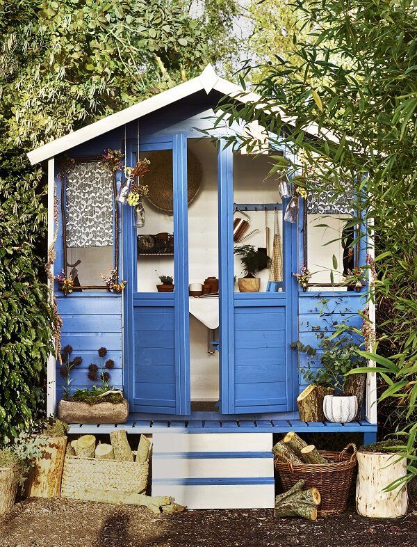 a small blue and white shed sitting in the middle of a garden with potted plants