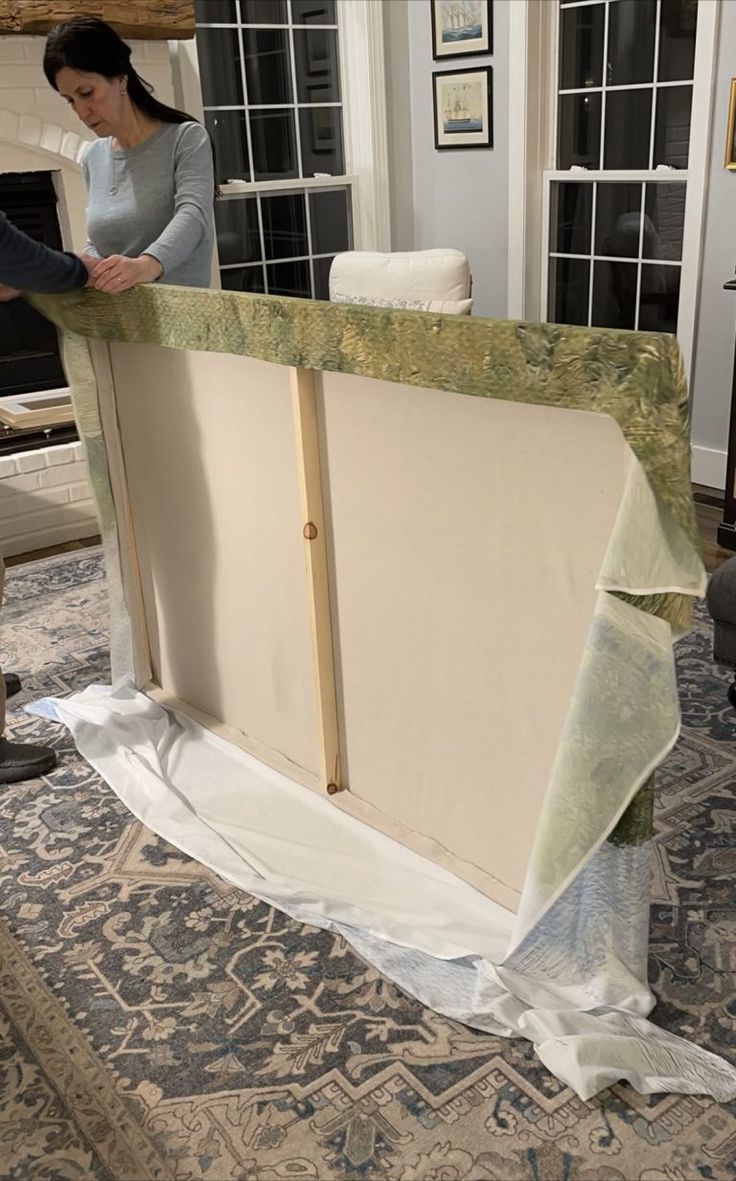 a woman standing next to a couch covered in sheeting on top of a rug