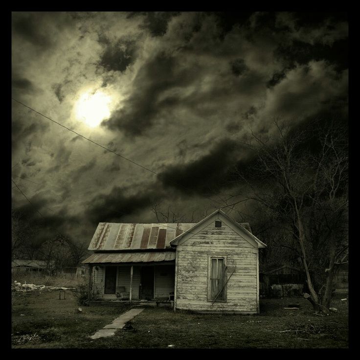 an old run down house sitting in the middle of a field under a cloudy sky