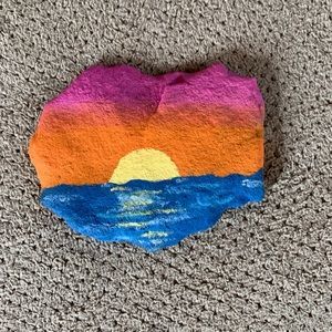 a painted rock sitting on top of a carpet covered in gray and orange colors with the sun setting behind it