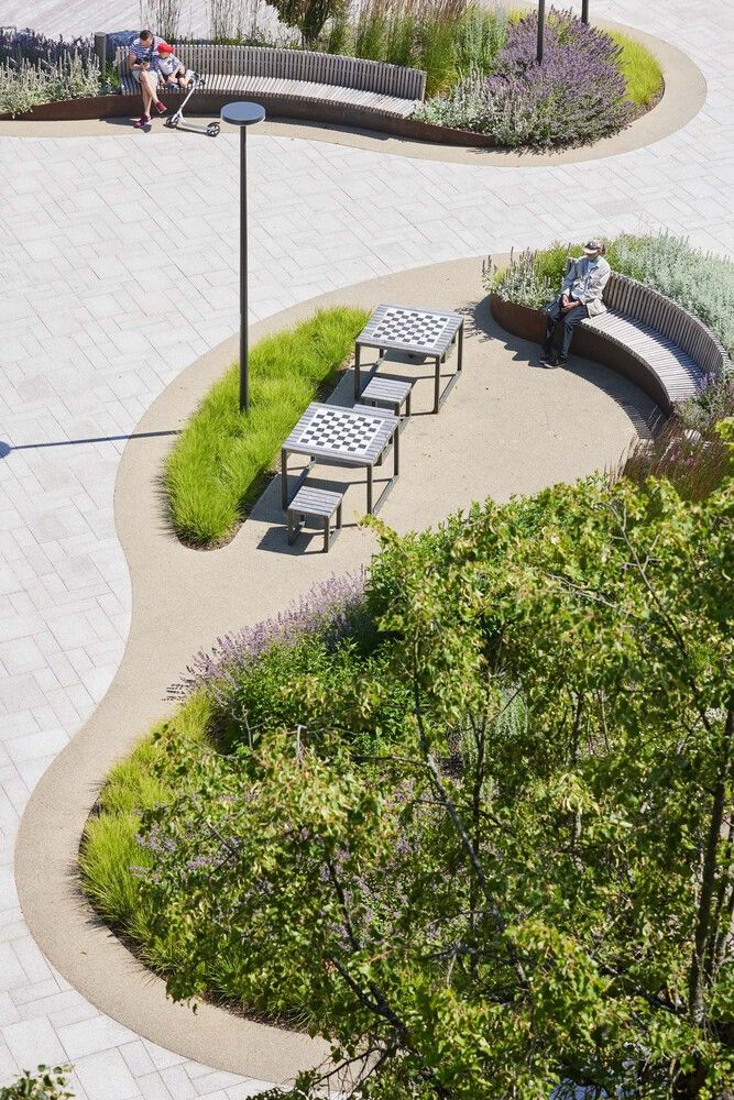 two people sitting on benches in the middle of a park with trees and plants around them