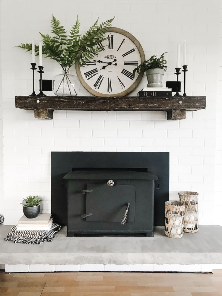 a fireplace with a clock above it and plants on the mantel shelf over it