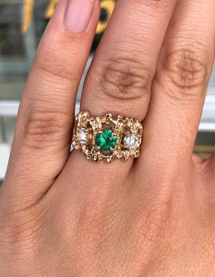 A vintage, unisex three stone emerald and diamond ring. Crafted in 14K yellow gold, a round natural emerald is prong-set alongside natural diamonds in a nugget-style ring. The earth mined gemstones are all clean to the eye and vivacious! The golden nugget design is seen on this solitaire piece and adds depth to the irregular design. A wide, smooth shank comfortably wraps around the finger. This is the perfect right-hand ring. 14K Yellow Gold OR White Gold Rhodium / 9.6 Grams Main Stone: Emerald 14k Gold Emerald Ring With 17 Jewels - Collectible, Heirloom Yellow Gold Cluster Ring For May Birthstone, Vintage Yellow Gold Three-stone Jewelry, Yellow Gold May Birthstone Collectible Ring, Vintage Yellow Gold Three Stone Jewelry, Heirloom Multi-stone Emerald Ring In Gold, Collectible Yellow Gold May Birthstone Ring, Collectible May Birthstone Yellow Gold Ring, Heirloom Three-stone Ring