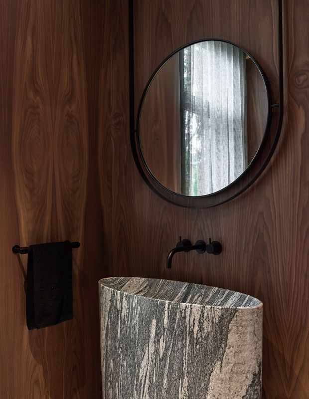 a round mirror hangs on the wall above a marble sink in a wood - paneled bathroom