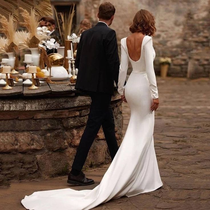 a man and woman walking down a cobblestone street holding hands while dressed in white