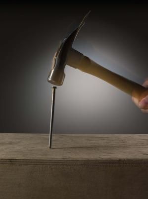 a person is holding a hammer over a block of wood with a knife stuck in it