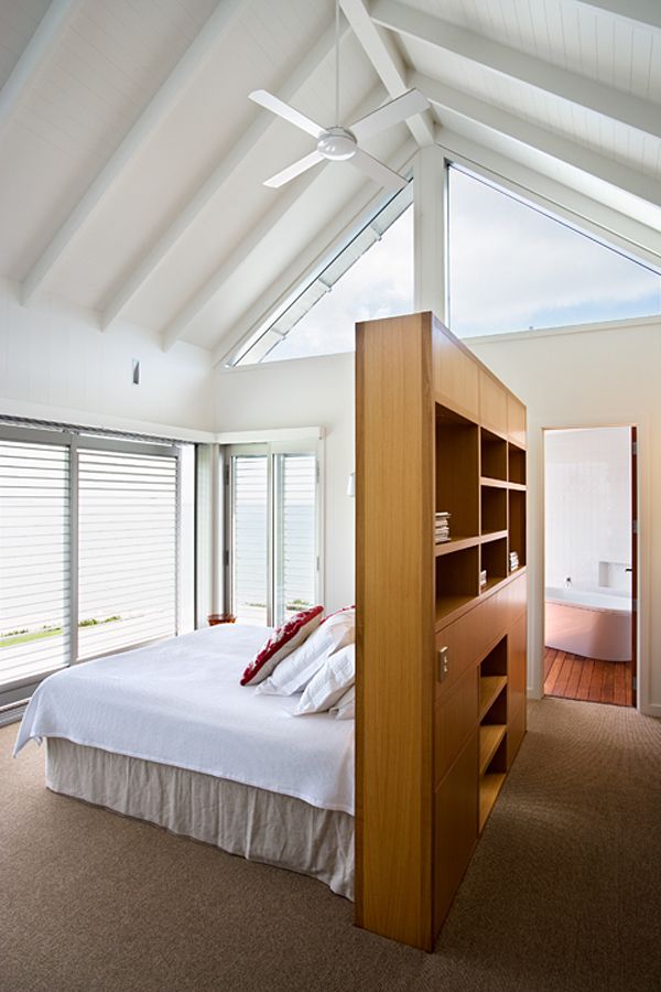 a large bed sitting under a window next to a wooden shelf filled with pillows and blankets