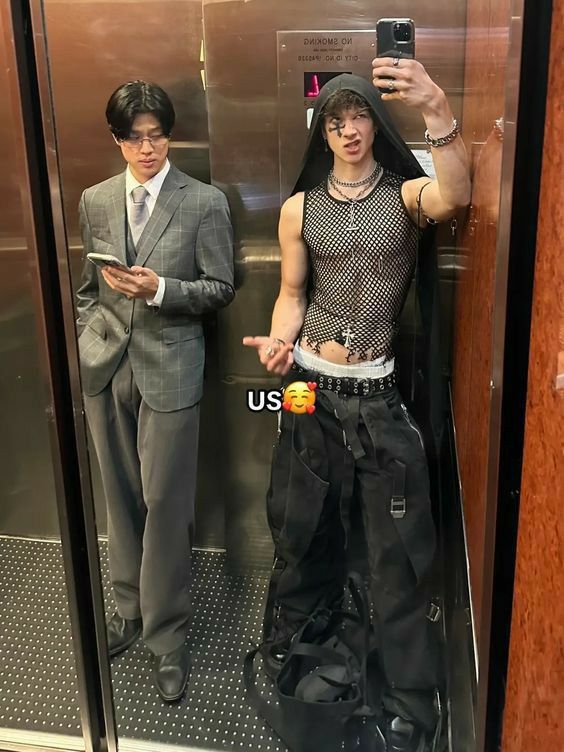 two men standing in an elevator with one taking a selfie and the other looking at his cell phone