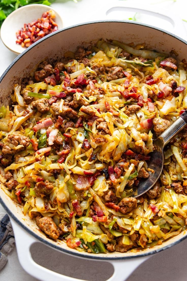 a pan filled with cabbage and meat on top of a white table next to some vegetables