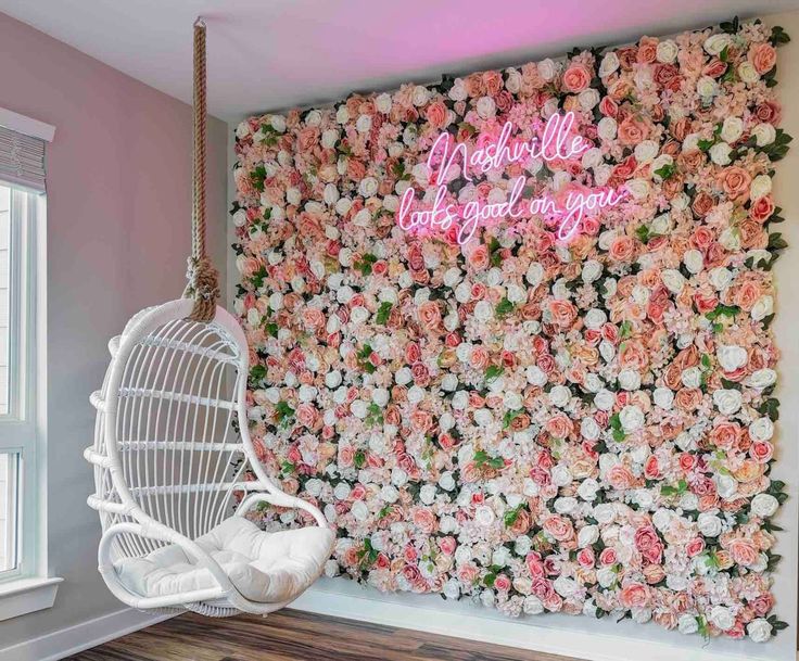 a white swing chair sitting in front of a flower covered wall