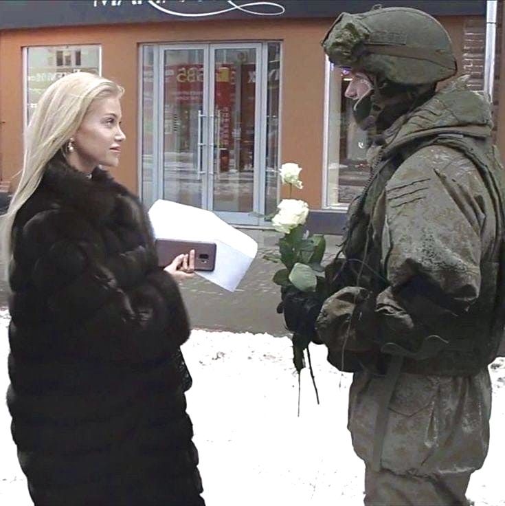 a man in winter clothes standing next to a woman holding a box with flowers on it