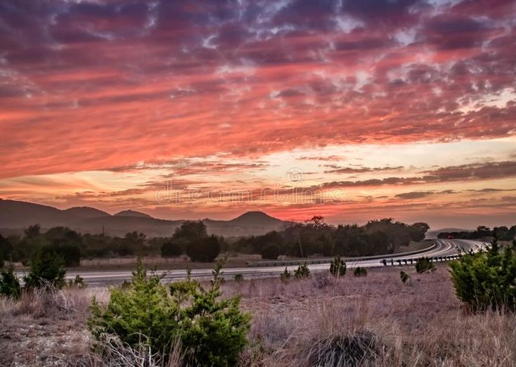 the sun is setting over an empty road in the desert with mountains in the background