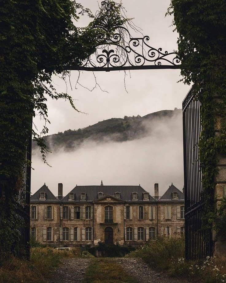 an iron gate leading to a large building with ivy growing on it's sides