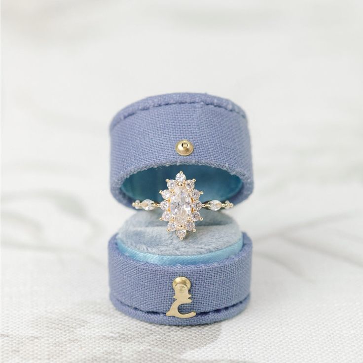 an engagement ring in a blue velvet box on a white cloth covered surface with gold accents