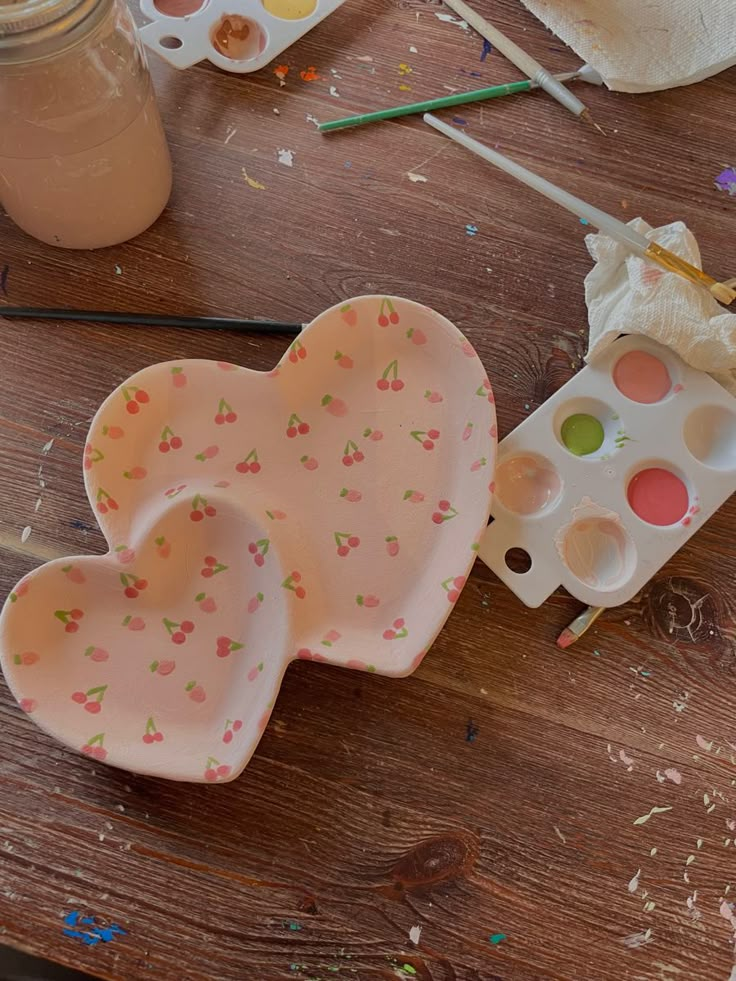 two heart shaped dishes sitting on top of a wooden table next to paintbrushes