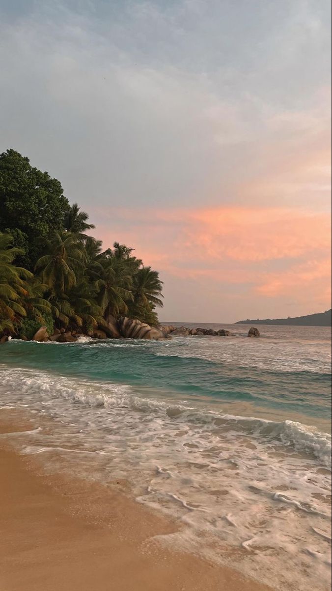 the beach has waves coming in to shore and palm trees lining the shoreline at sunset