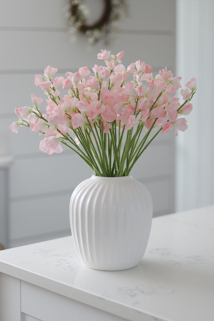 a white vase filled with pink flowers on top of a table