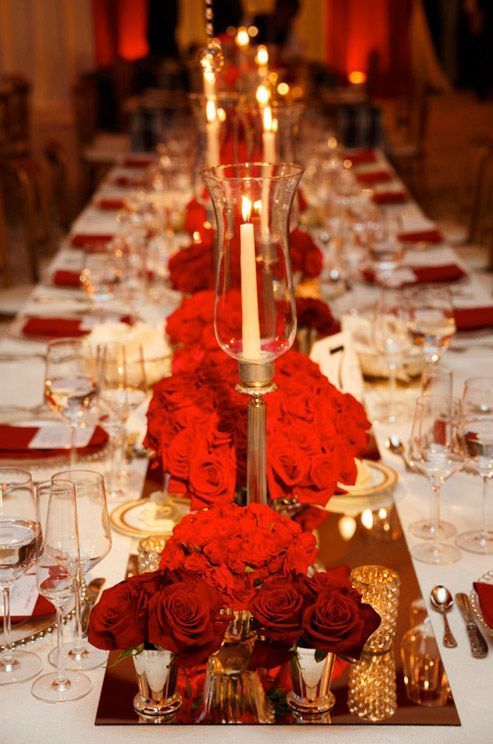 a long table is set with red roses and candles for an elegant dinner or party