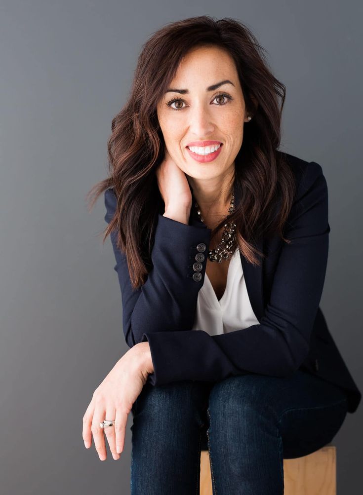 a woman sitting on top of a wooden chair with her hand on her chin and looking at the camera