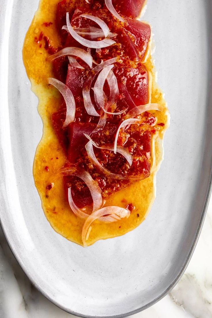 a white plate topped with meat and onions on top of a marble countertop next to a knife