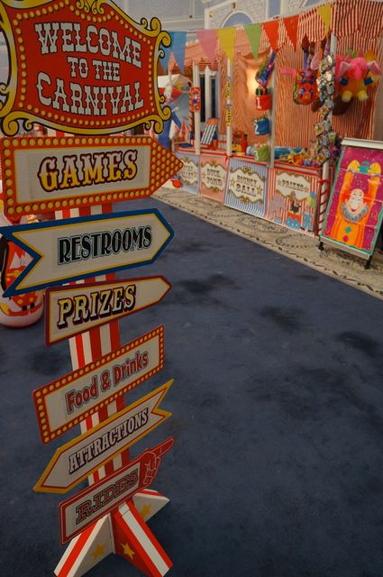 a street sign in front of a carnival with many signs pointing to different places and destinations