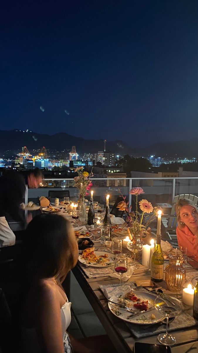 a group of people sitting around a table with food and drinks on it at night