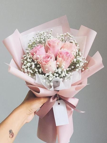 a hand holding a bouquet of pink roses with baby's breath in the middle